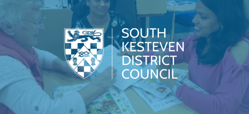 Photograph of women sat at a table, discussing language lessons. Blue screen overlaid on screen. South Kesteven District Council logo in the centre. 